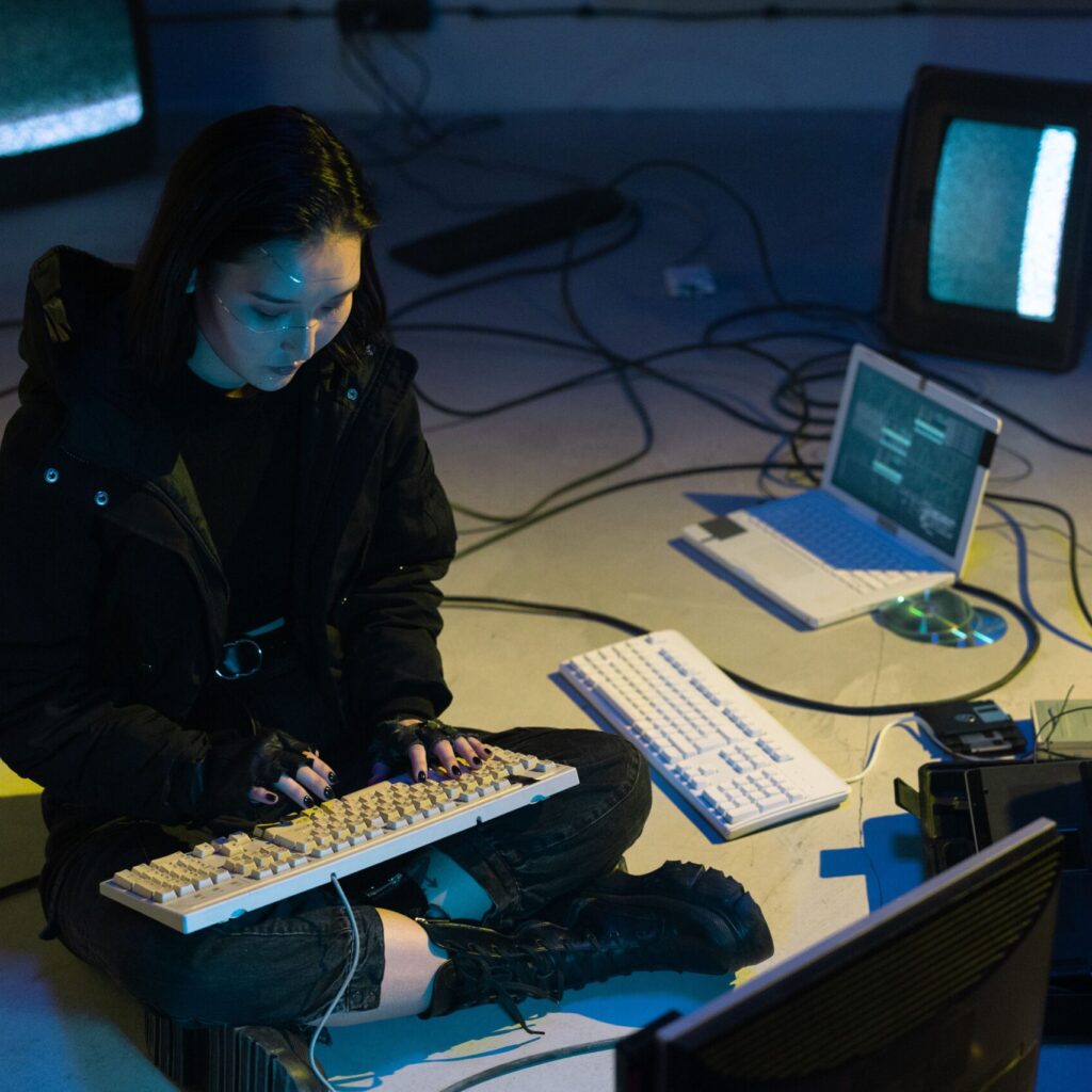 Young Asian woman engaged in computer hacking in a dimly lit, technologically equipped room.